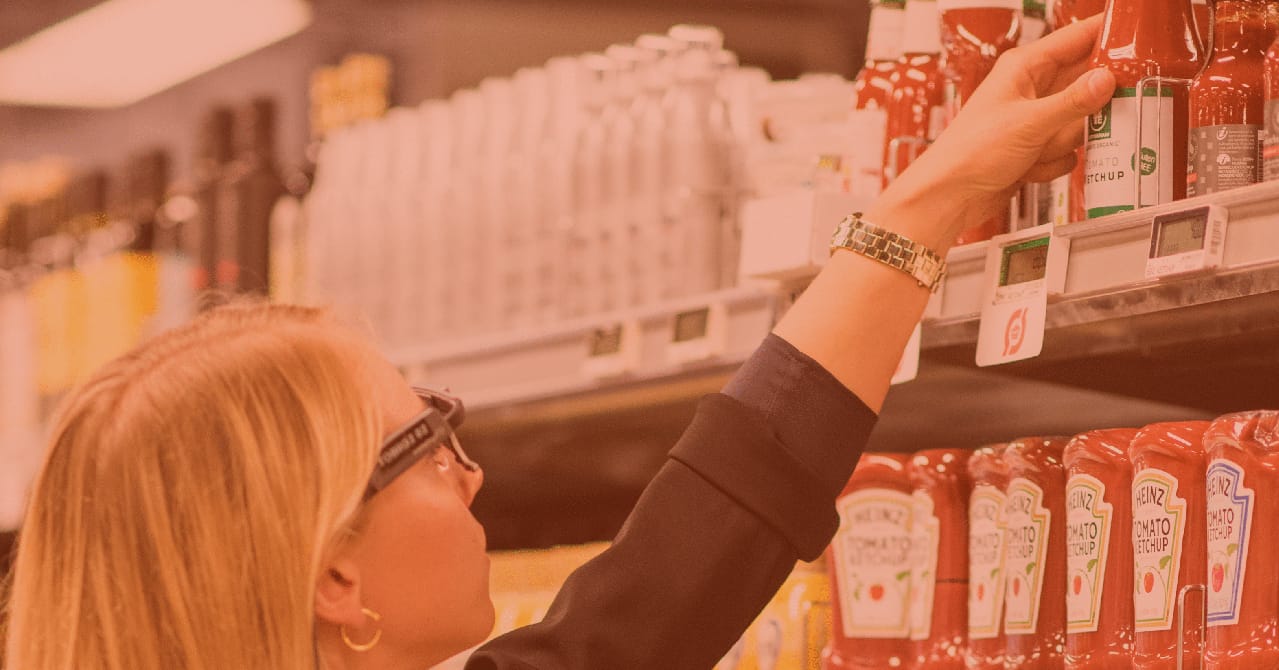 Woman in supermarket reaching for ketchup while wearing eye tracking glasses