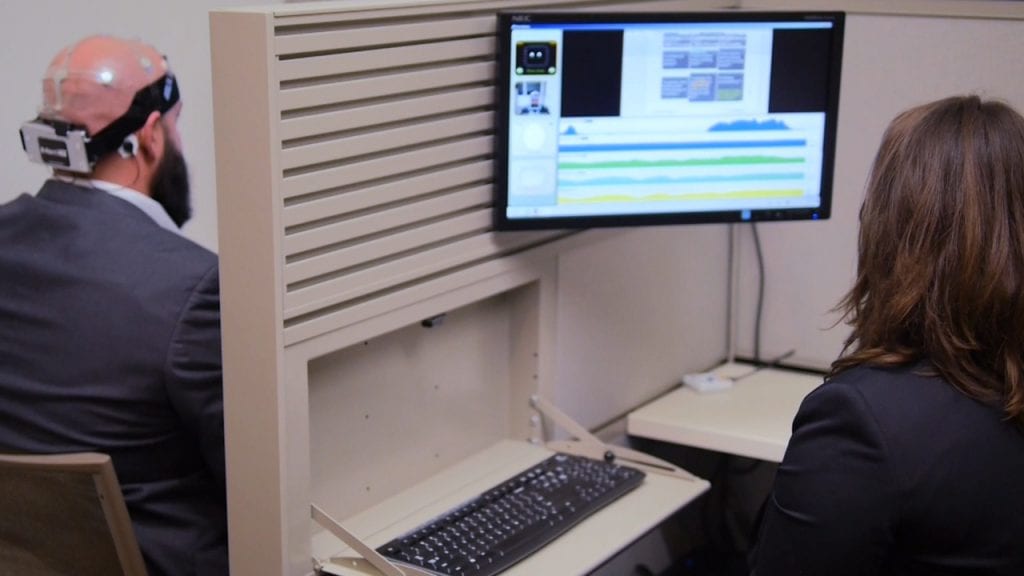 man wearing a eeg headset wall in between and woman looking at a screen