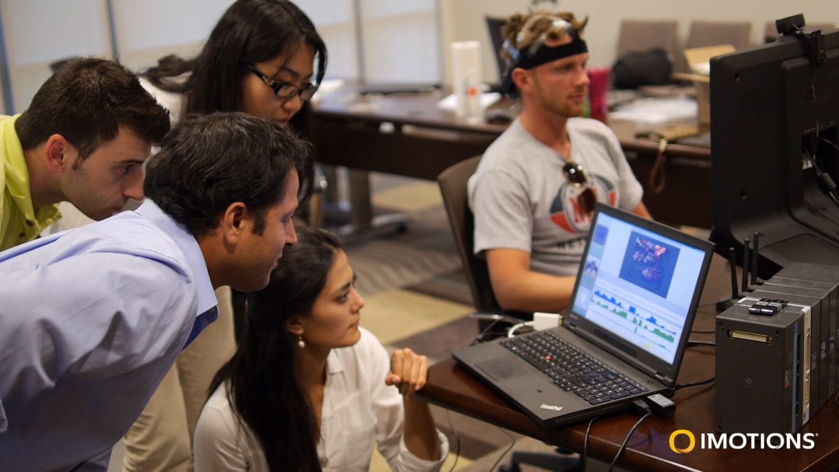 man wearing an eeg headset and two women and two man looking at a computer screen for the results