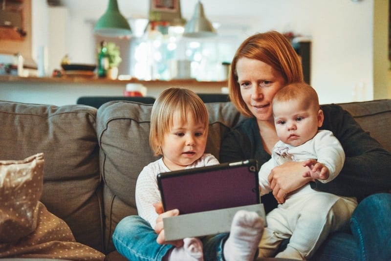 mom sitting on a couch with two small children all looking at a tablet screen